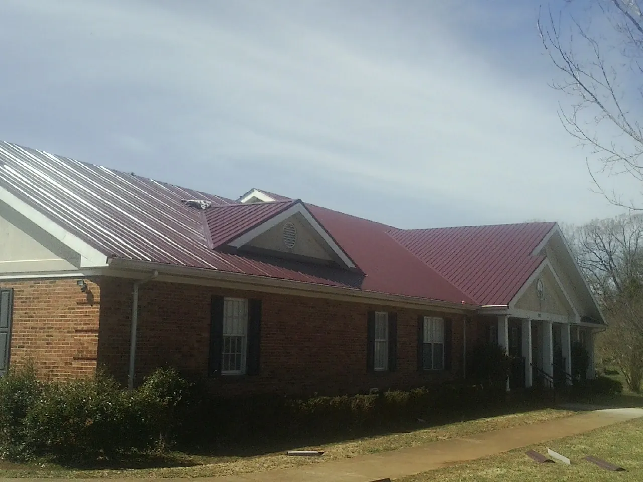 Red metal roof with gabled entries on a long brick building, from a Hail Damage Roof Repair job in Elmira