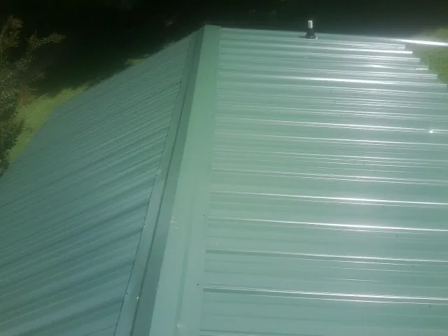 New green metal panels meeting at the ridge of a roof — Flat Roof Repair work by our crew in Elmira